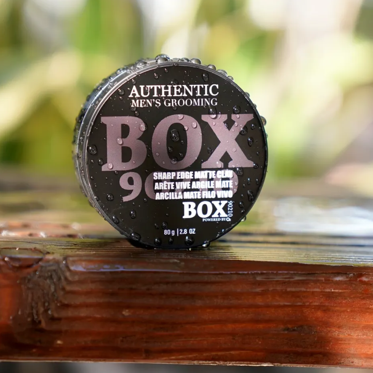 Cylindrical container labeled 'BOX 9' on a wooden surface with a blurred natural background