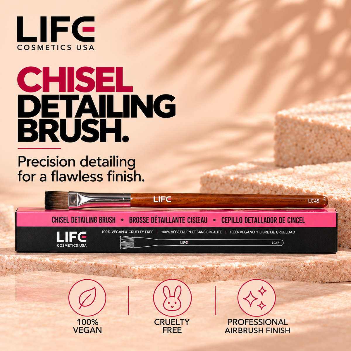 LIFE Cosmetics USA LC45 Chisel Detailing Brush with a wooden handle, silver ferrule and flat dark bristles resting on its pink-and-black box on a peach stone surface.