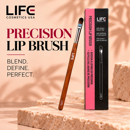 LIFE Cosmetics USA LC55 Precision Lip Brush with rounded dark bristles, a silver ferrule and wooden handle leaning beside its upright pink-and-black box on a peach stone surface.