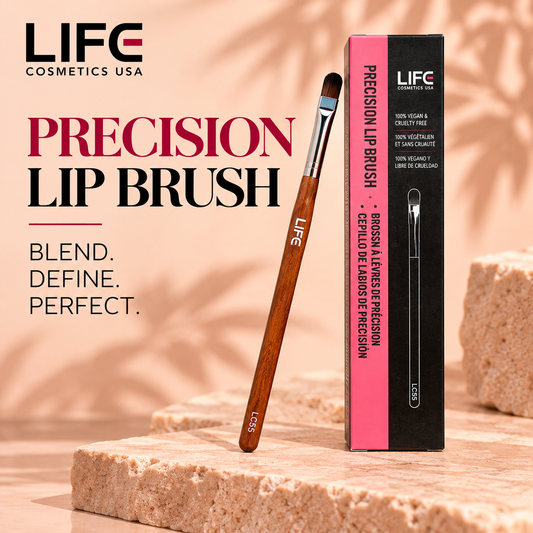LIFE Cosmetics USA LC55 Precision Lip Brush with rounded dark bristles, a silver ferrule and wooden handle leaning beside its upright pink-and-black box on a peach stone surface.