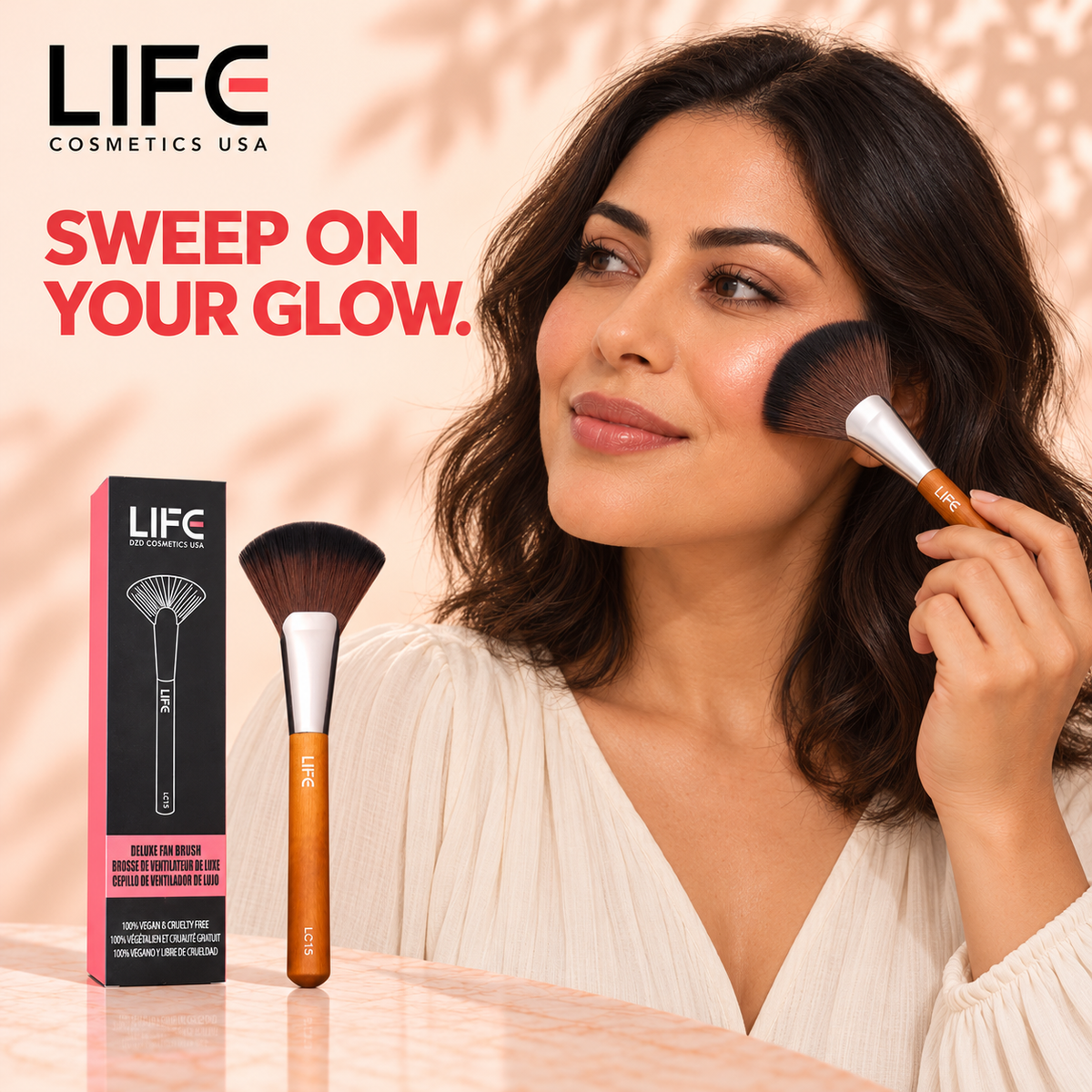 Woman applying makeup to her cheek with the LIFE Cosmetics USA LC15 Deluxe Fan Brush, beside the brush and retail box.