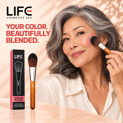 Woman with wavy gray hair applying makeup with the LIFE Cosmetics USA LC11 Medium Oval Brush, beside the brush and retail box.