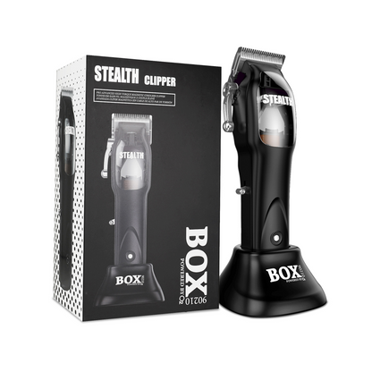 Black BOX90210 STEALTH clipper with silver blades standing in its charging base beside the branded retail box on white.