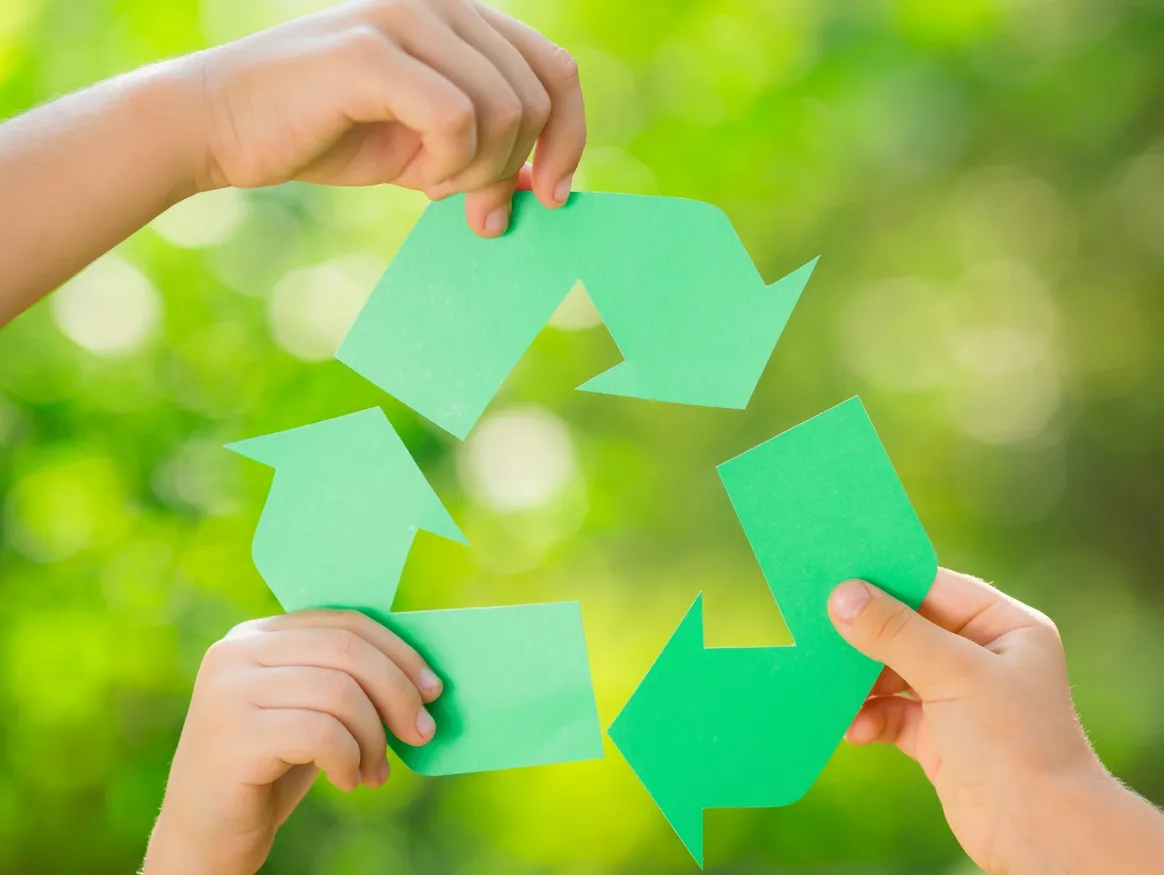 Three hands holding green paper recycling symbols against a blurred natural background