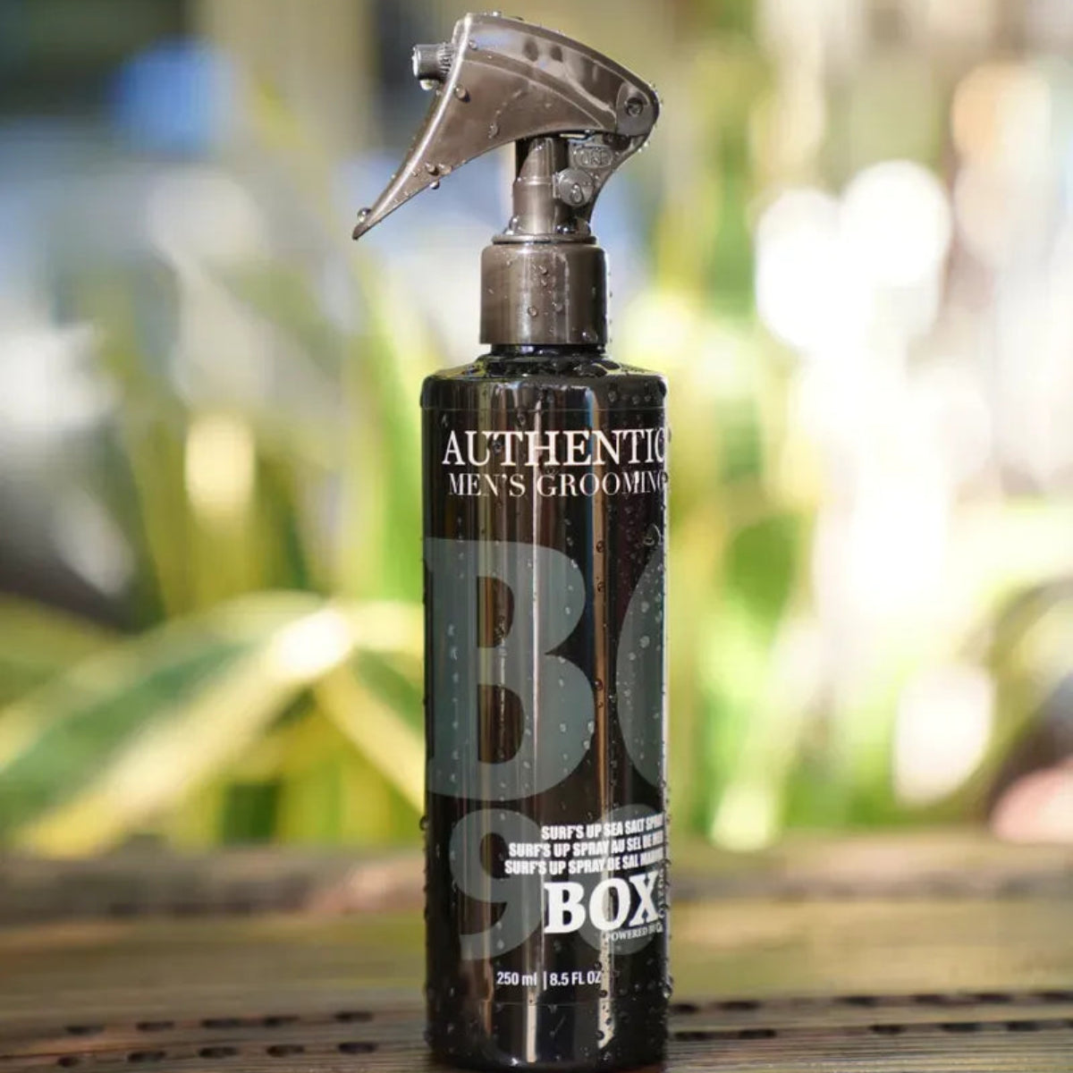 Spray bottle labeled 'Authentic Men's Grooming Box' on a wooden surface with a blurred natural background