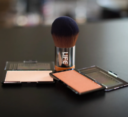 Makeup brush and compact powders on a dark surface with a blurred background
