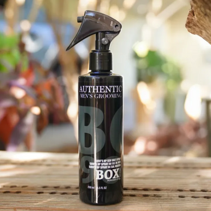 Black spray bottle labeled 'BO Box' on a wooden surface with a blurred outdoor background