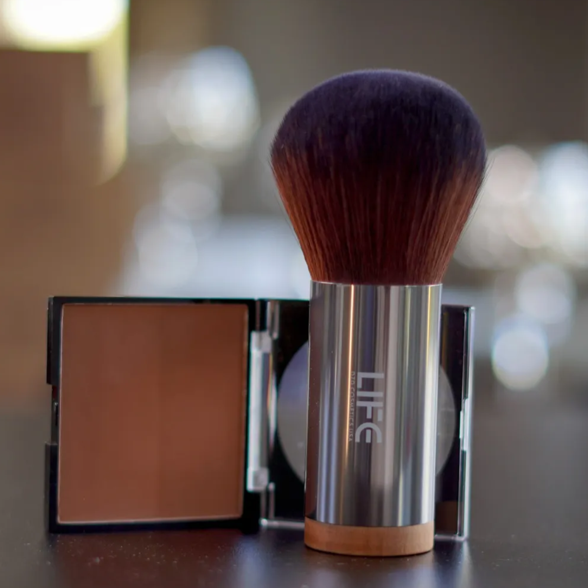 Makeup brush and compact powder with 'LIFE' branding on a blurred background