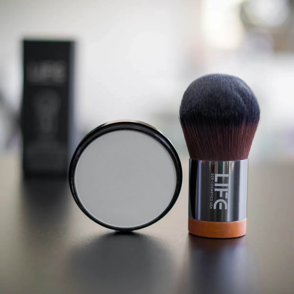 Makeup brush and compact powder with 'LIFE' branding on a reflective surface.