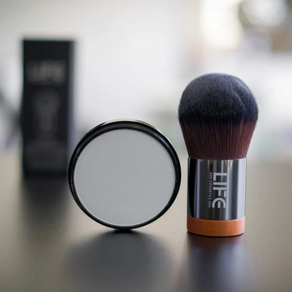 Makeup brush and compact powder with 'LIFE' branding on a reflective surface.